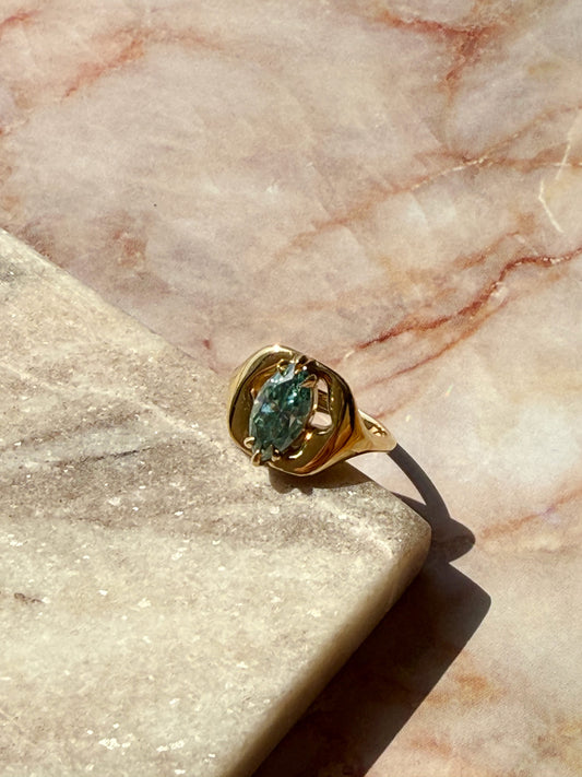 Gold ring with a green gemstone on a marble surface