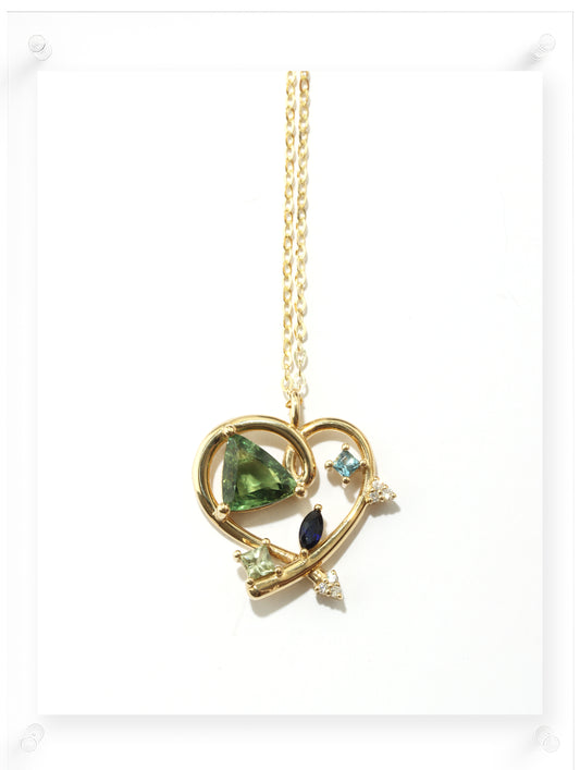 Gold necklace with a heart-shaped pendant featuring green, black, and blue gemstones on a white background.