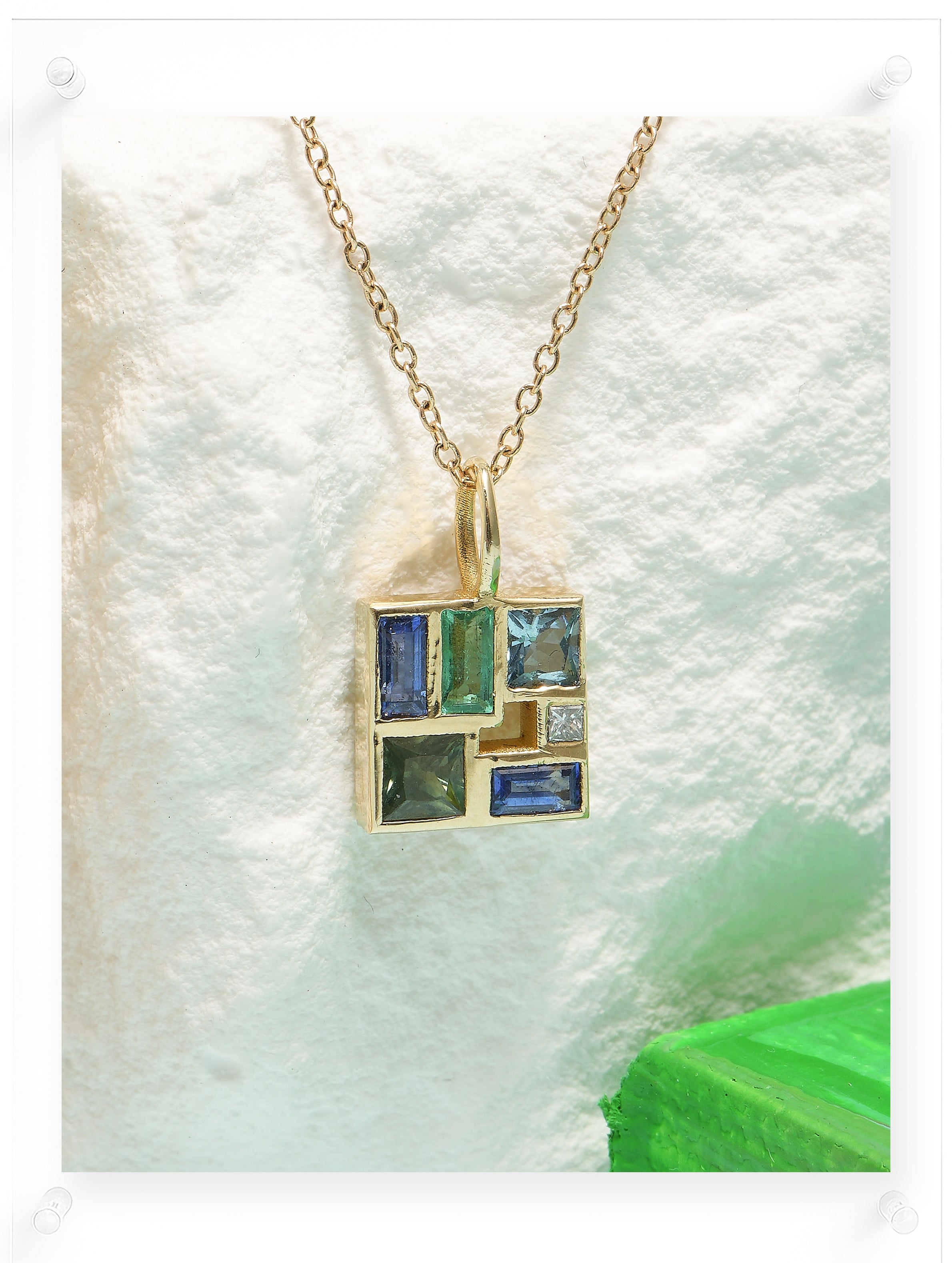 Gold necklace with a pendant featuring green and blue gemstones on a white background