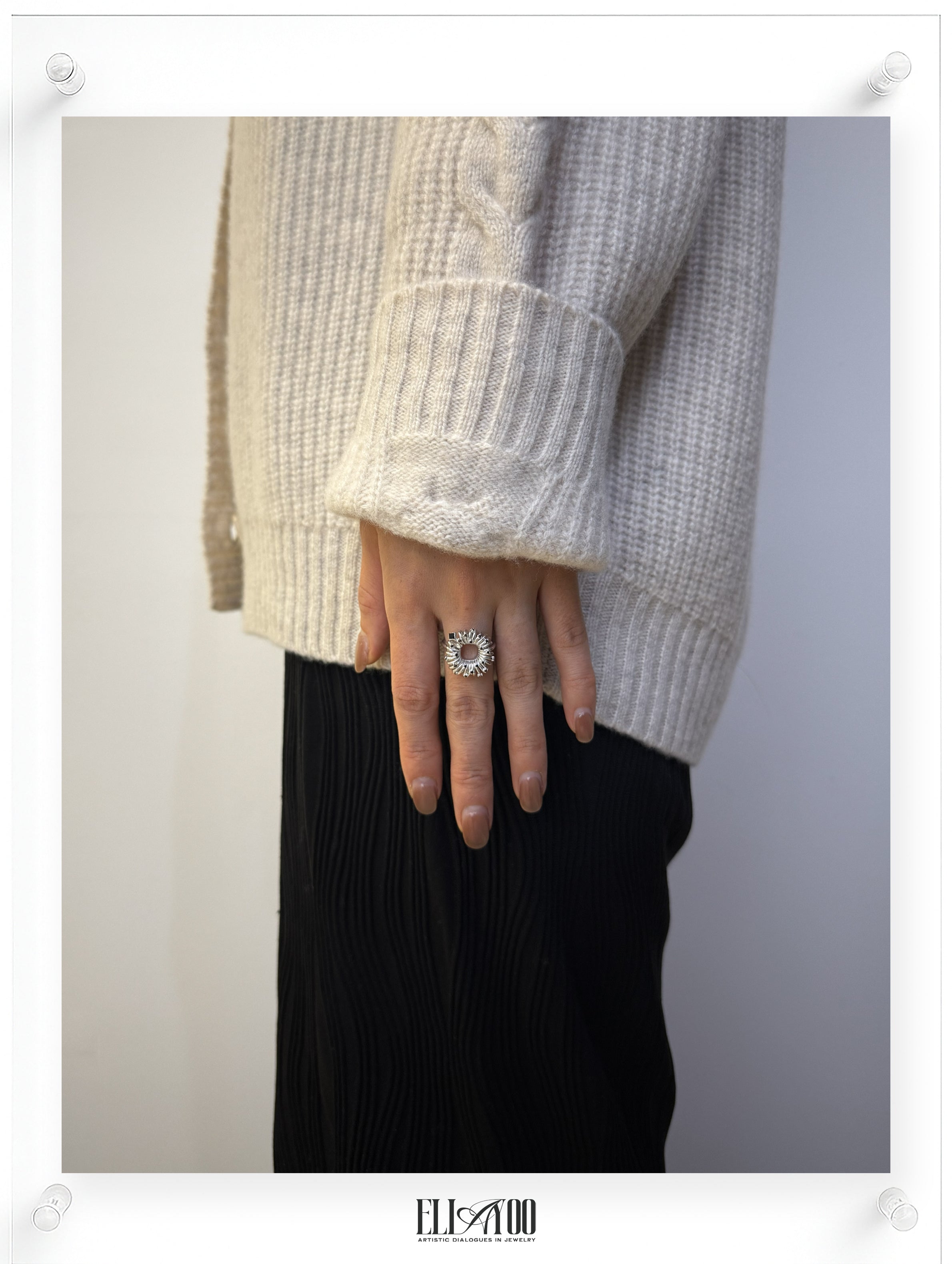 Model wearing sculptural silver ring with circular petal setting and black diamond accents