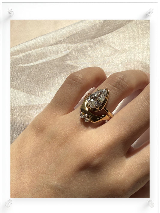 Yellow gold pear-shaped diamond ring with a sculptural flowing setting, worn on hand in soft natural light against sheer fabric