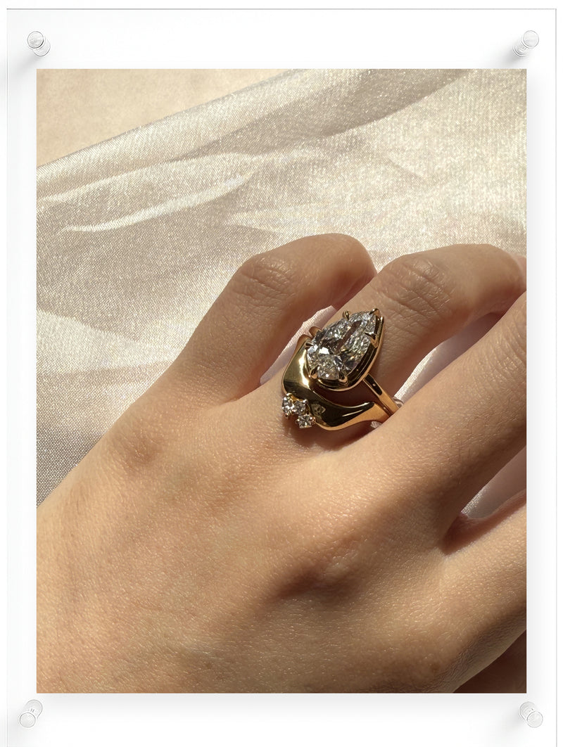 Yellow gold pear-shaped diamond ring with a sculptural flowing setting, worn on hand in soft natural light against sheer fabric