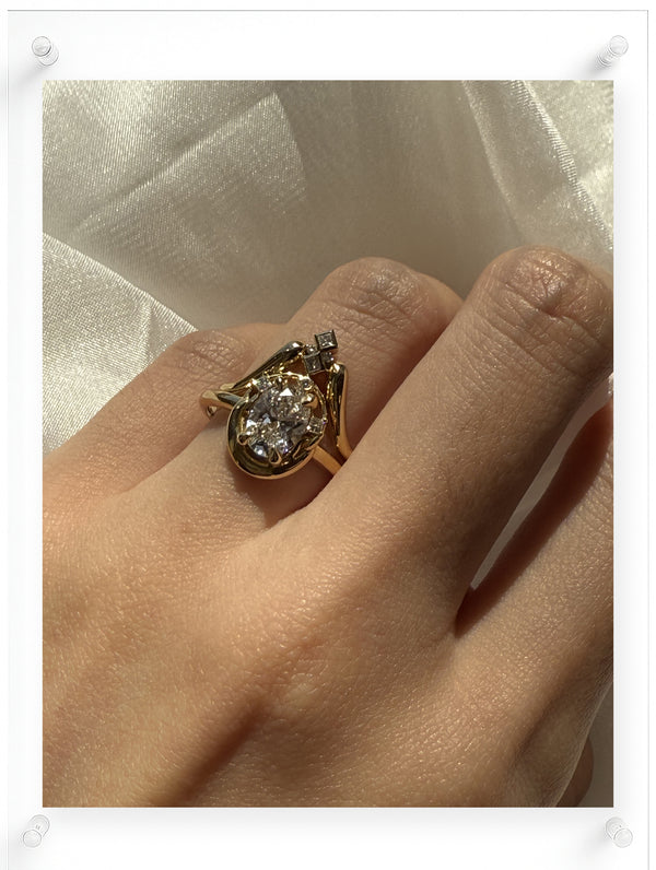 Model wearing a yellow gold oval diamond ring with sculptural setting and accent diamonds, captured in natural light on the hand