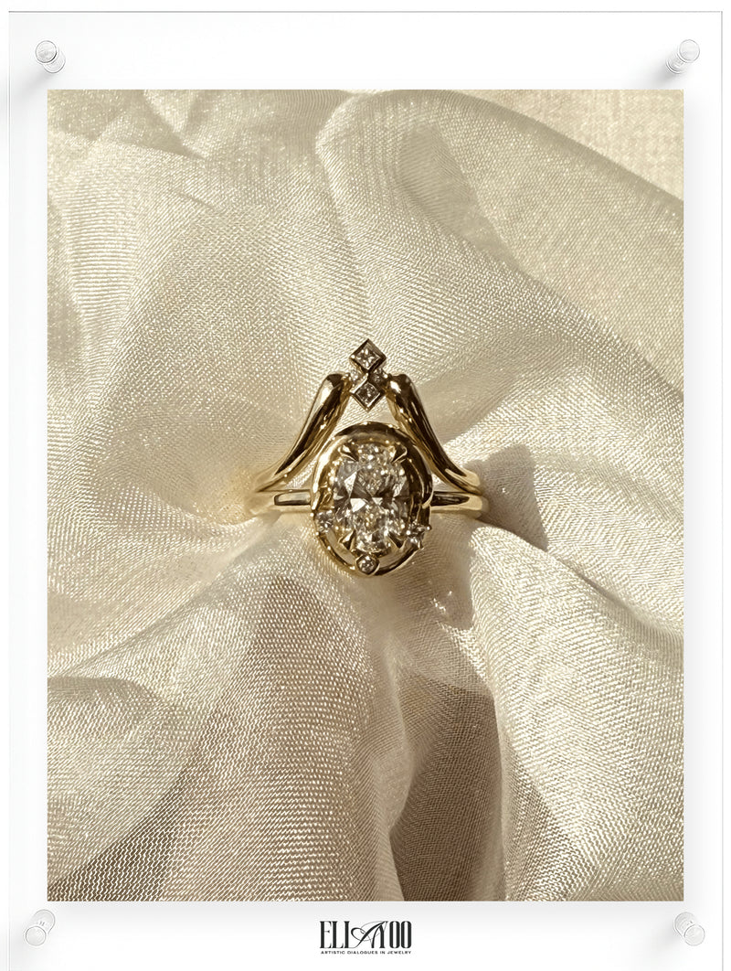 Yellow gold oval diamond ring with sculptural setting and accent diamonds, photographed on soft ivory fabric in natural light