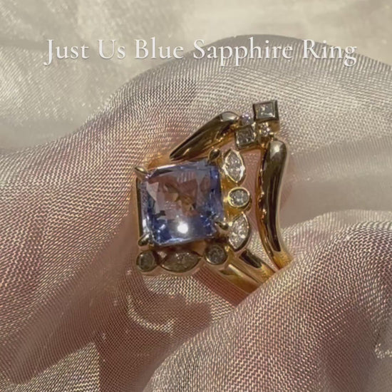 video showing Gold ring with a blue gemstone and smaller diamonds on a white fabric background