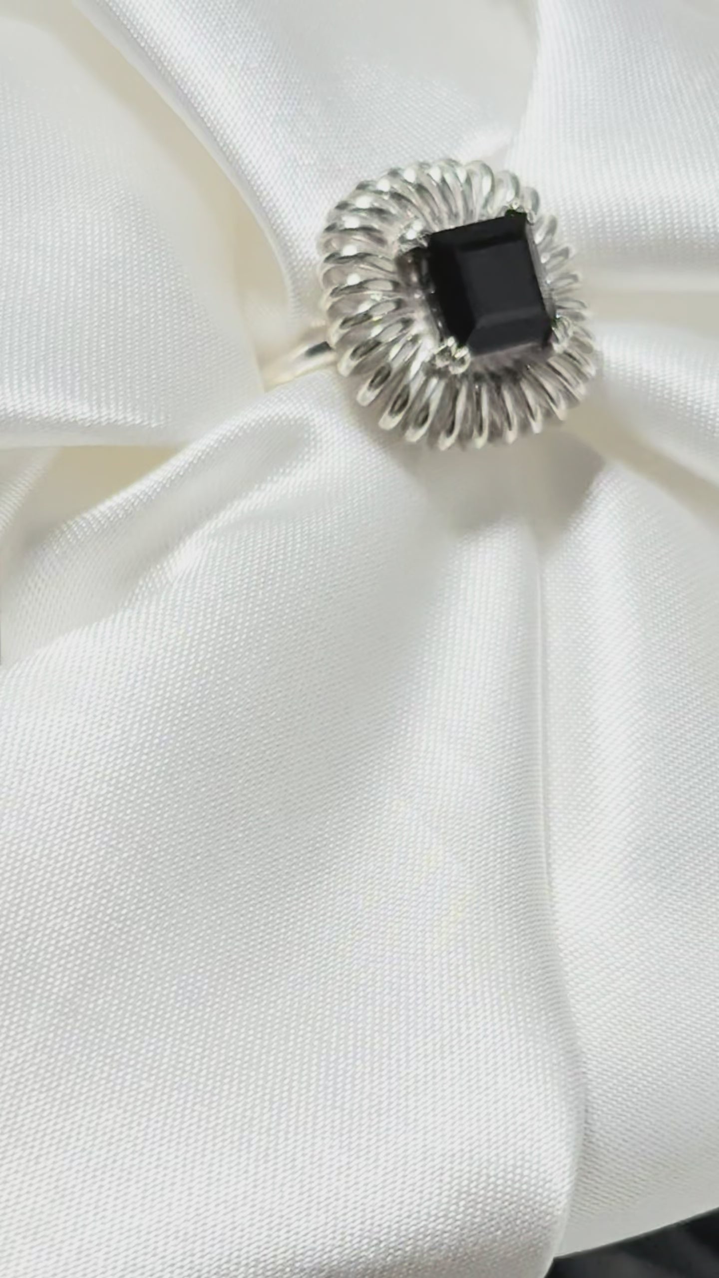 Princess cut onyx ring displayed on silk fabric, sculptural silver petal setting